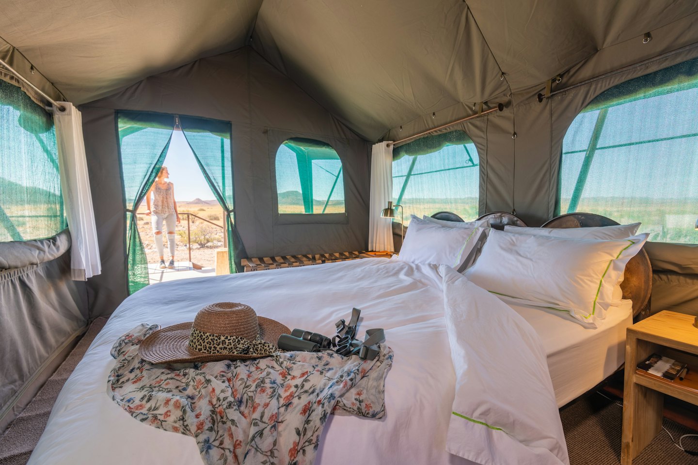 Donna guarda fuori da una tenda da safari su un paesaggio arido.