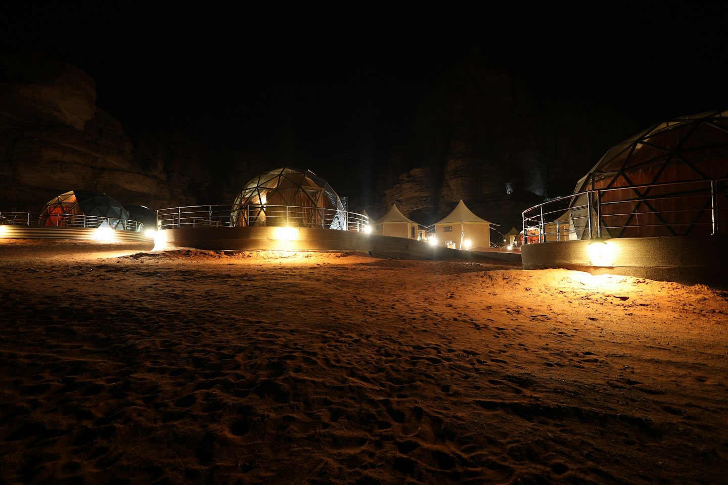 Cupole e tende geodetiche illuminate su terreno sabbioso di notte.